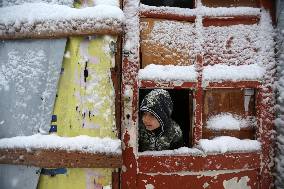 A
Syrian
boy
looks
out
through
his
tent
door
covered
in
snow
at
a
refugee
camp
in
Deir
Zannoun
village,
in
the
Bekaa
valley,
east
Lebanon. Picture of the Day for January 8, 2015.