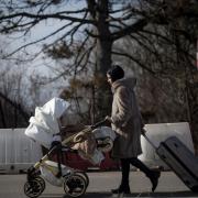 A woman pushes a baby stroller after crossing the border from Ukraine at the Romanian-Ukrainian border, in Siret, Romania, Friday, Feb. 25, 2022. Thousands of Ukrainians are fleeing from war by crossing their borders to the west in search of safety. They