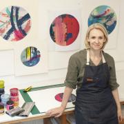 Kate Watkins artist standing in front of a wall of brightly coloured circle screenprints