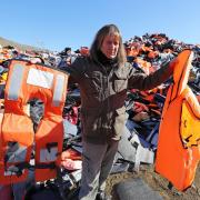 British expatriate Eric Kempson, who is battling to save lives on the Greek island of Lesbos, holds a life jacket next to a fake life jacket (right) as he stands between piles of used life jackets, which he said the majority of  which are fake.