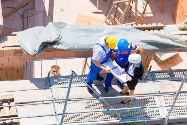 Construction site Team or architect and builder or worker with helmets discuss on a scaffold construction plan or blueprint or checklist.